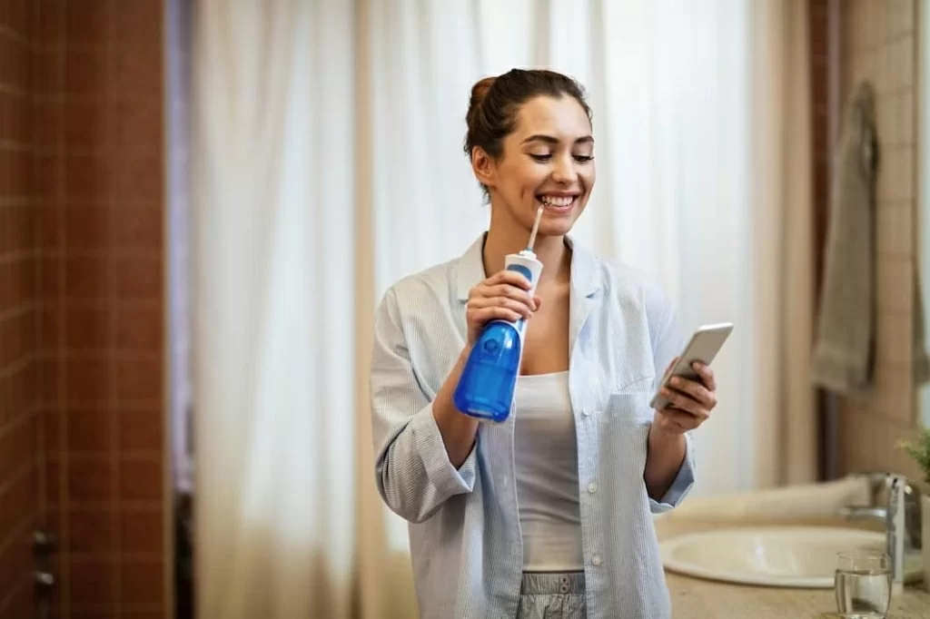 young-happy-woman-using-dental-water-flosser-cleaning-her-teeth-while-texting-mobile-phone-bathroom_.jpg