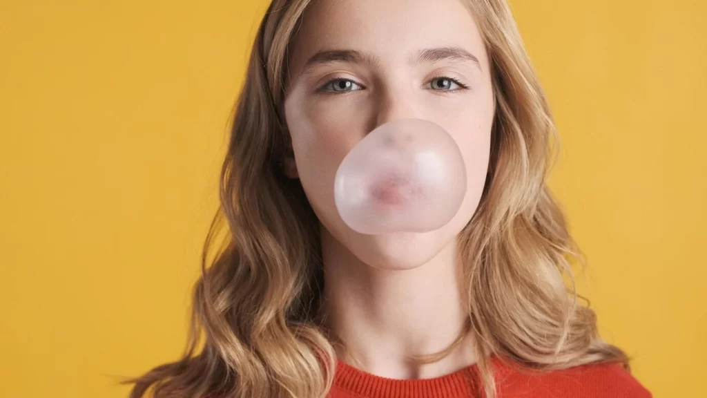 close-up-pretty-blond-teenager-girl-with-wavy-hair-blowing-bubble-from-gum-camera-yellow-background-candy-bubble_574295-4198.jpg